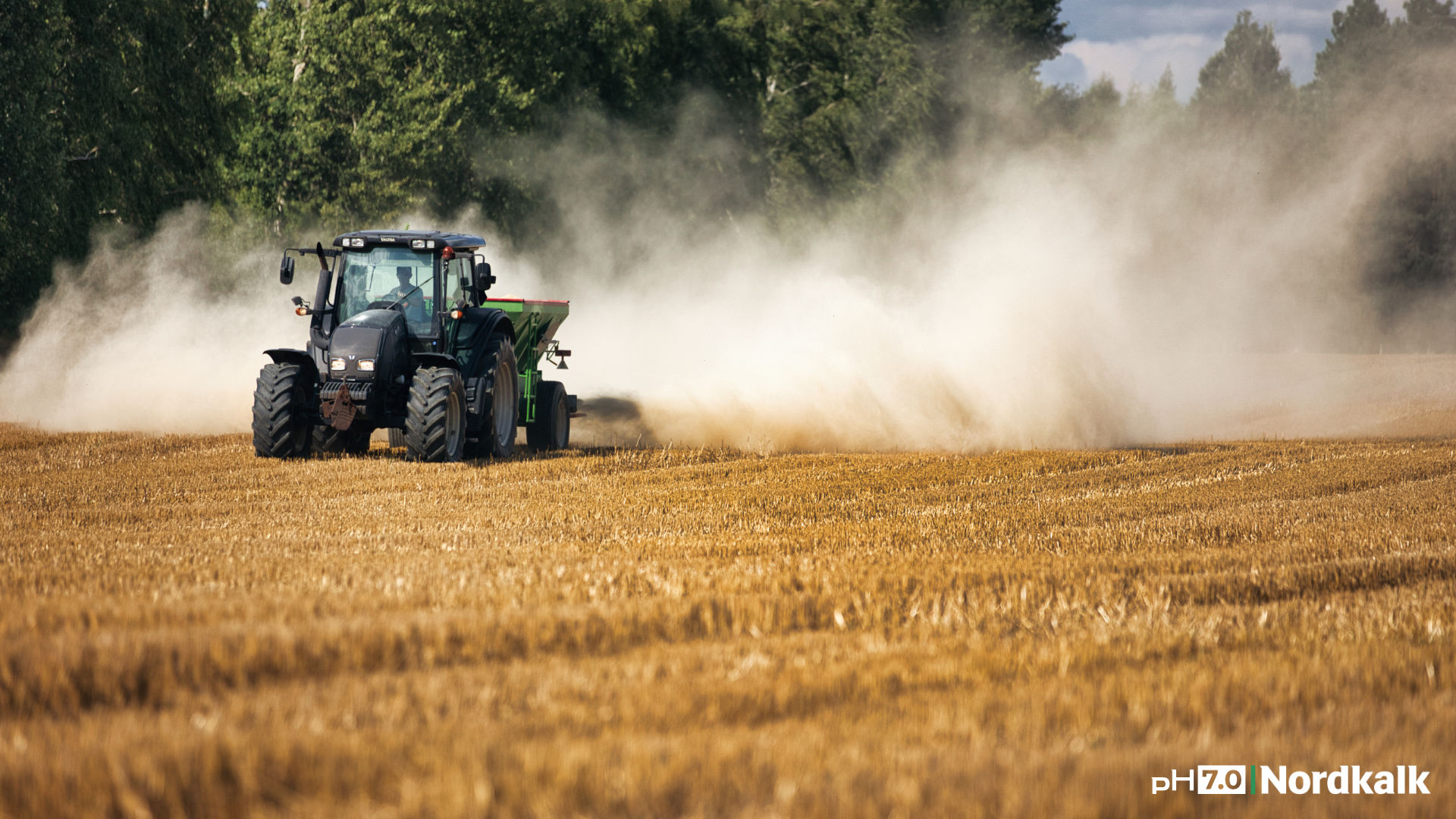 Ciągnik z rozsiewaczem rozsiewa wapno.